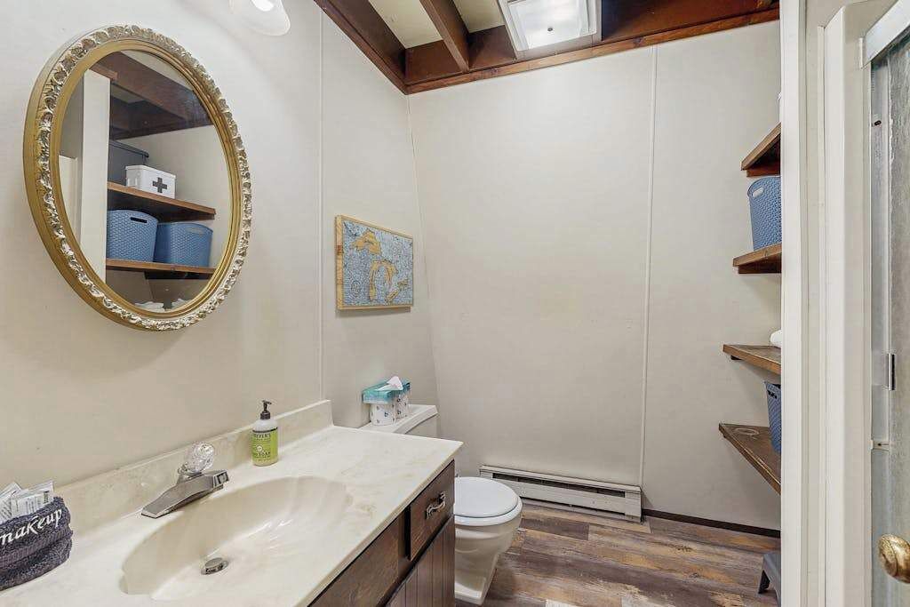 A bathroom with a sink, mirror, toilet, and storage shelves.