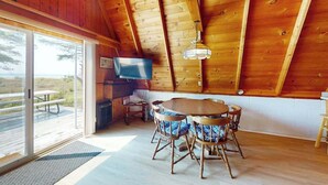 Un intérieur en bois comprenant un coin repas, un téléviseur et une vue dégagée grâce à de grandes fenêtres.
