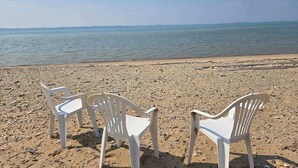 Une plage avec trois chaises en plastique blanches, disposées face à la mer.