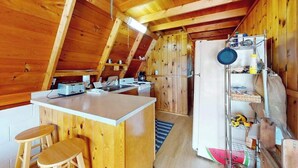 Une cuisine compacte aux murs en bois, dotée d’un plan de travail blanc et d’un petit coin repas avec des tabourets.