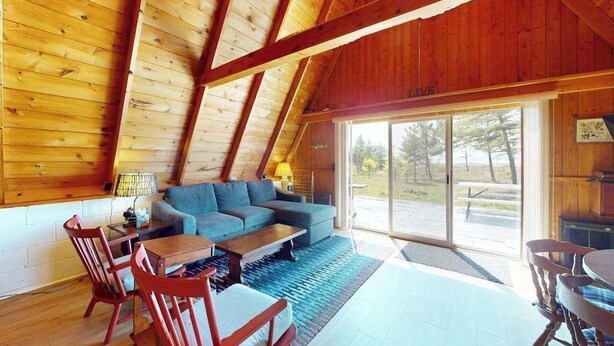 L’intérieur d’un chalet accueillant, avec un plafond en bois, un canapé bleu, une table à manger et des chaises.