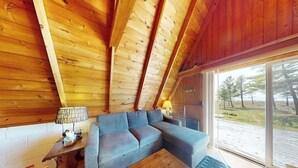 Un intérieur en bois avec un canapé, une table et une vue sur l’extérieur, visible à travers une grande fenêtre.
