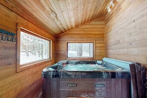 A wooden cabin interior with a hot tub, large windows, and a sloped ceiling. - Resort home with private indoor hot tub, game room, firepit, bikes, Ping-Pong (Thompsonville)
