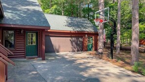 A log cabin with a basketball hoop, a garage, and a green door. - Resort home with private indoor hot tub, game room, firepit, bikes, Ping-Pong (Thompsonville)
