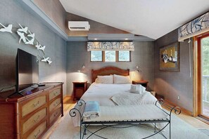 A bedroom with a bed, dresser, TV, and artwork. - Lakefront condo with deck, gorgeous view, fireplace, & W/D (Glen Arbor)