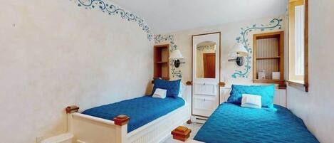 A bedroom with two beds, a ceiling fan, a door with a mirror, and a small trash bin.