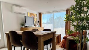 Uma área de refeições com uma mesa de madeira, cadeiras, uma televisão e um vaso com planta.