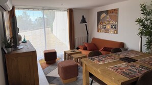 Uma sala de estar moderna com sofá, pufes, uma mesa de jantar e uma janela grande.