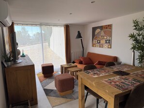Ein modernes Wohnzimmer mit einer Couch, Hocker, einem Esstisch und einem großen Fenster.