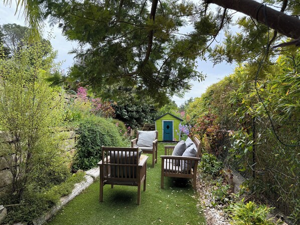 Ein Garten mit einer Holzbank, einem kleinen grünen Schuppen und üppiger Bepflanzung.