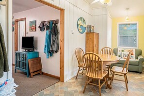 A dining area with a wooden table and chairs, a television on a cabinet, and a green sofa with a beach-themed pillow.