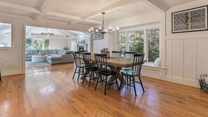 Een eetgedeelte met een houten tafel en stoelen, een kroonluchter en uitzicht op een woonkamer met een bank en een open haard.