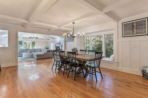 Ein Essbereich mit Holztisch und -stühlen, einer Kristallleuchter und Blick auf ein Wohnzimmer mit Sofa und Kamin.