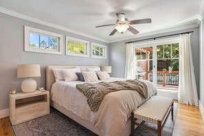 Ein Schlafzimmer mit Bett, Nachttisch, Lampe, Deckenventilator und großen Fenstern.