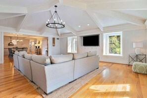 Un salon spacieux avec un grand canapé d’angle, un lustre et un téléviseur.