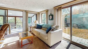 A spacious living room with a large window, a sofa, a coffee table, and a chair. - Riverfront Cabin with Stunning Views, Fire pit, Gas Grill & WIFI (Thompsonville)