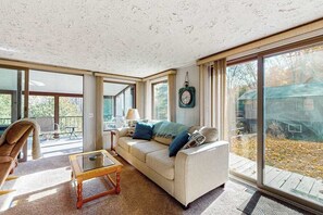 A spacious living room with a large window, a sofa, a coffee table, and a chair. - Riverfront Cabin with Stunning Views, Fire pit, Gas Grill & WIFI (Thompsonville)