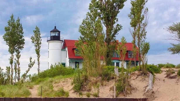 A lighthouse with a red roof, a white building with green trim, and a sandy beach with sparse vegetation. - Riverfront Cabin with Stunning Views, Fire pit, Gas Grill & WIFI (Thompsonville)
