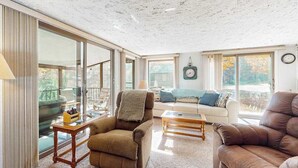 A spacious living room with large windows, a sofa, a recliner, and a coffee table. - Riverfront Cabin with Stunning Views, Fire pit, Gas Grill & WIFI (Thompsonville)