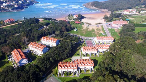 An aerial view of a coastal resort with multiple buildings, a beach, and a mountainous backdrop. - Duplex with view La Arena 4605 (Arnuero)