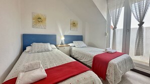 A room with two beds, a nightstand, a lamp, and a window with curtains. - Duplex with view La Arena 4605 (Arnuero)