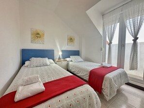 A room with two beds, a nightstand, a lamp, and a window with curtains. - Duplex with view La Arena 4605 (Arnuero)