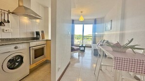 A kitchen with a washing machine, oven, and a dining area with a checkered tablecloth. - Duplex with view La Arena 4605 (Arnuero)