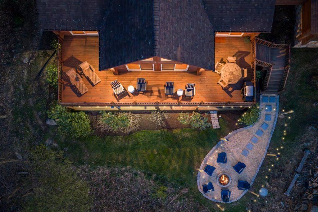 An aerial view of a wooden deck with outdoor seating, a fire pit, and a curved pathway.