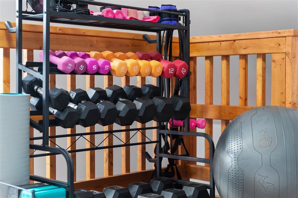 A multi-tiered dumbbell rack with various weights, a yoga mat, and a wooden wall in the background.