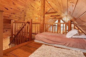 Une chambre dans une cabane en bois, avec un lit, un tapis blanc et un escalier en bois.