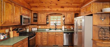 A wooden cabin interior with a kitchen featuring wooden cabinets, a microwave, stove, refrigerator, and a sink.