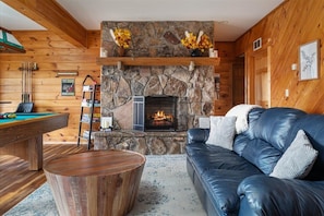 A cozy room with a stone fireplace, a pool table, a leather sofa, and a wooden coffee table. - Lakeview Log Cabin - Deep Creek Lake - Hot Tub, Fire Pit, Lake Views, Sleeps 14 (Swanton)