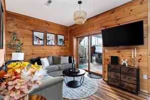 A wooden interior with a sofa, a TV, and a staircase leading outside. - Lakeview Log Cabin - Deep Creek Lake - Hot Tub, Fire Pit, Lake Views, Sleeps 14 (Swanton)