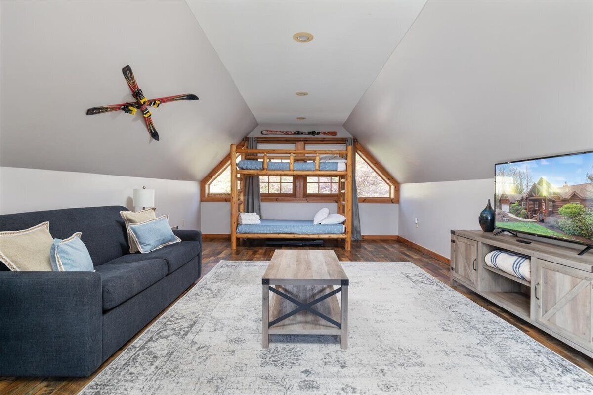 A loft-style room with a bunk bed, a sofa, a coffee table, and a TV on a wooden cabinet.