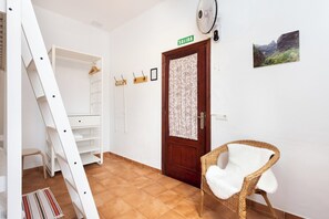 A room with a white wardrobe, a wicker chair, a wooden door with a 'SALIDA' sign, a fan, and a framed picture on the wall. - TenoHomes Tabaiba Guesthouse, Tarucho (Buenavista del Norte)