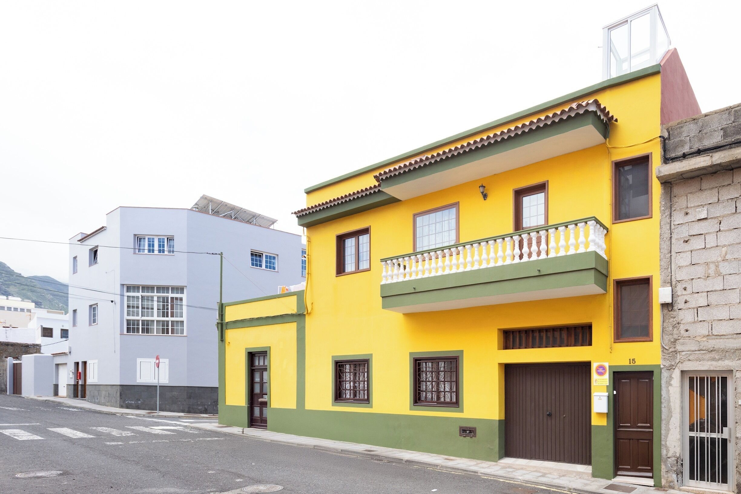 Um edifício amarelo com varanda, porta de garagem e o número 15 na lateral.