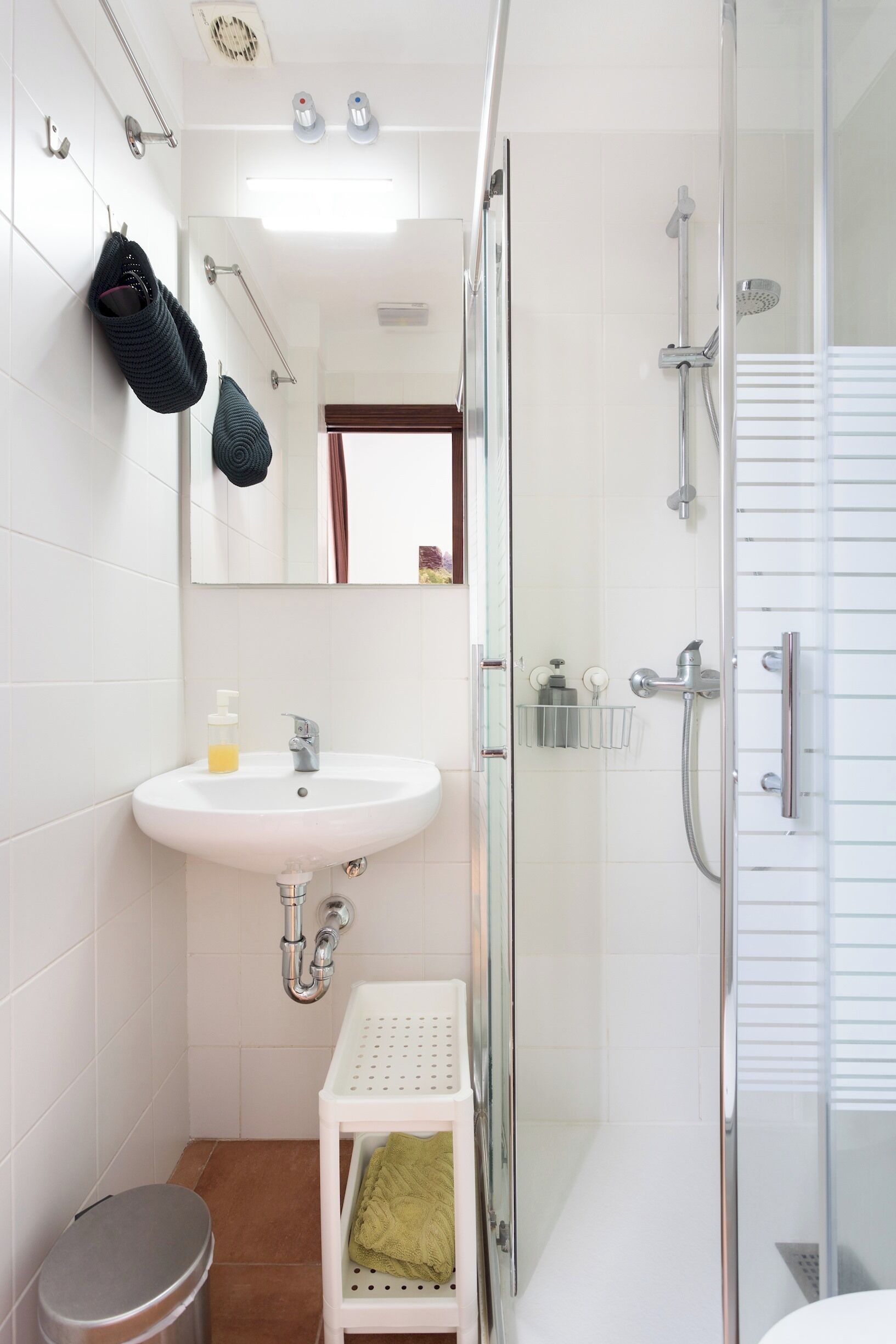 A bathroom with a white sink, a glass shower enclosure, a white toilet, and a small stool.