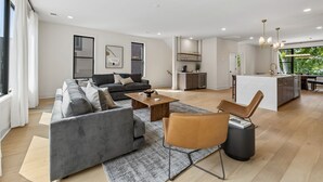 Una sala de estar moderna con sofá, mesa de centro y comedor, con una cocina al fondo.