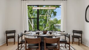 Comedor con una mesa redonda, sillas y vistas a árboles a través de amplias ventanas.