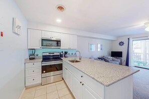A modern kitchen with white cabinets, a built-in microwave, and a large island with a sink. - Comfortable condo with deck, heated pool, and family-friendly amenities (Ocean City)