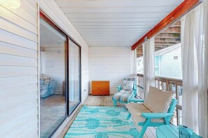 A covered porch with a sliding glass door, a wooden bench, and a small table. - Comfortable condo with deck, heated pool, and family-friendly amenities (Ocean City)