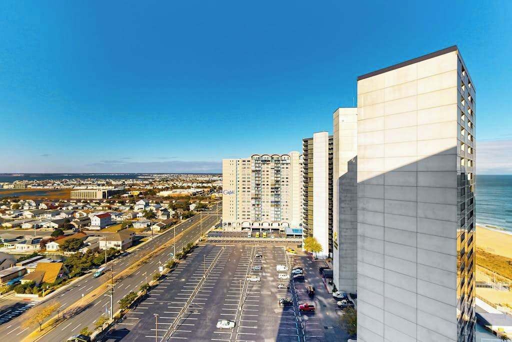 Ein Hochhaus mit Parkplatz davor, blauem Himmel und Blick auf den Strand.