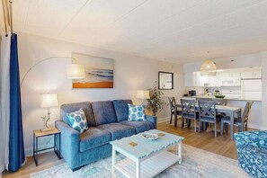 A living room with a sofa, coffee table, and dining area with chairs and a table. - Oceanfront Condo w/ Balcony & Amazing Beach Views (Ocean City)