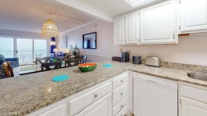 A modern kitchen with white cabinets, granite countertops, and a dining area with a table and chairs. - Oceanfront Condo w/ Balcony & Amazing Beach Views (Ocean City)