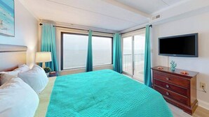 A hotel room with a bed, a TV, a dresser, and a balcony with curtains. - Oceanfront Condo w/ Balcony & Amazing Beach Views (Ocean City)