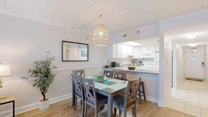 A modern kitchen with white cabinets, a dining area with a table and chairs, and a hanging light fixture. - Oceanfront Condo w/ Balcony & Amazing Beach Views (Ocean City)
