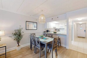 A modern kitchen with white cabinets, a dining area with a table and chairs, and a hanging light fixture. - Oceanfront Condo w/ Balcony & Amazing Beach Views (Ocean City)