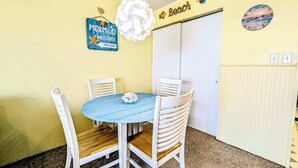 A room with a round table and four chairs, a white door, and wall decorations including a clock and a sign that says 'MERMAID WATCHING'. - Decatur House 207 (Ocean City)