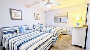 A bedroom with two beds, a ceiling fan, a window with blinds, and a small white dresser. - Decatur House 207 (Ocean City)