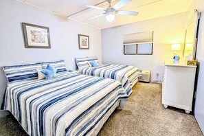 Ein Schlafzimmer mit zwei Betten, einem Deckenventilator, einem Fenster mit Jalousien und einer kleinen weißen Kommode.